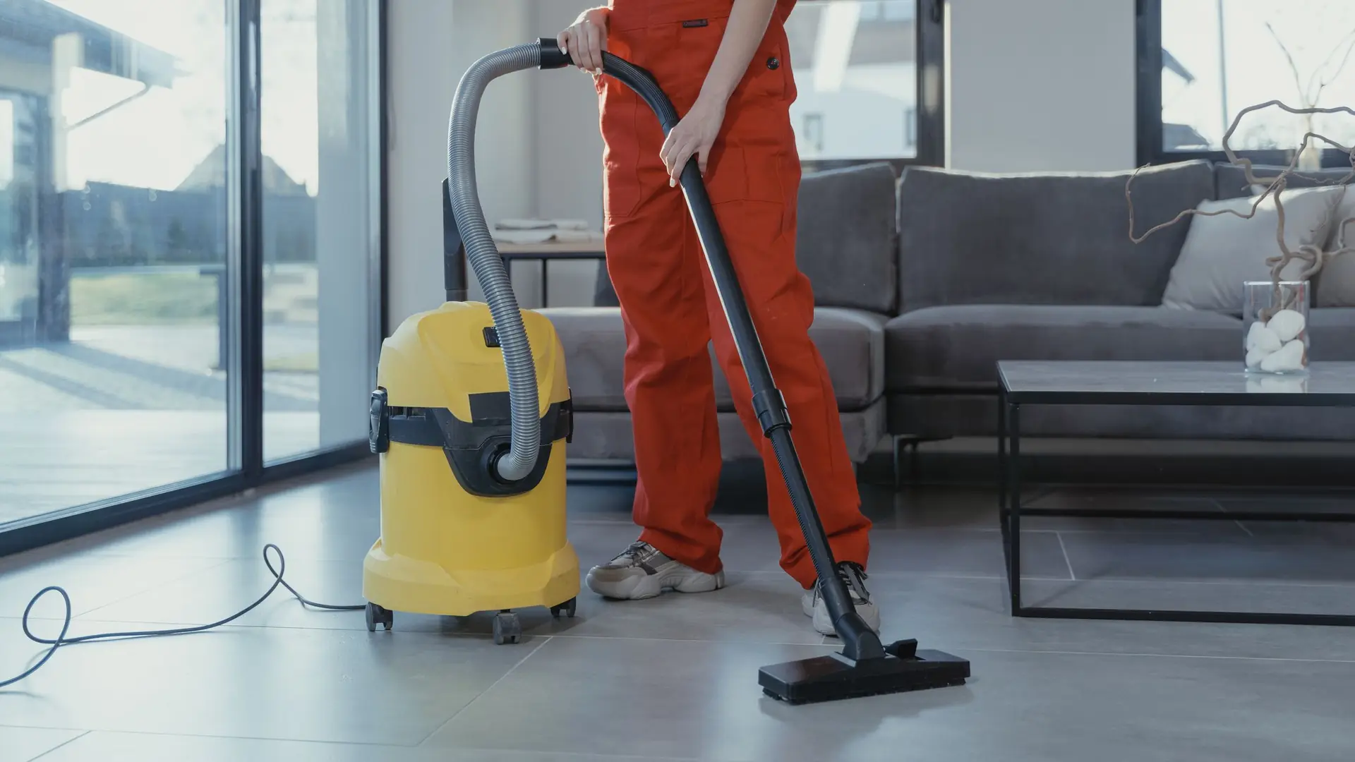 Profissional aspirando o piso de uma sala ampla e iluminada