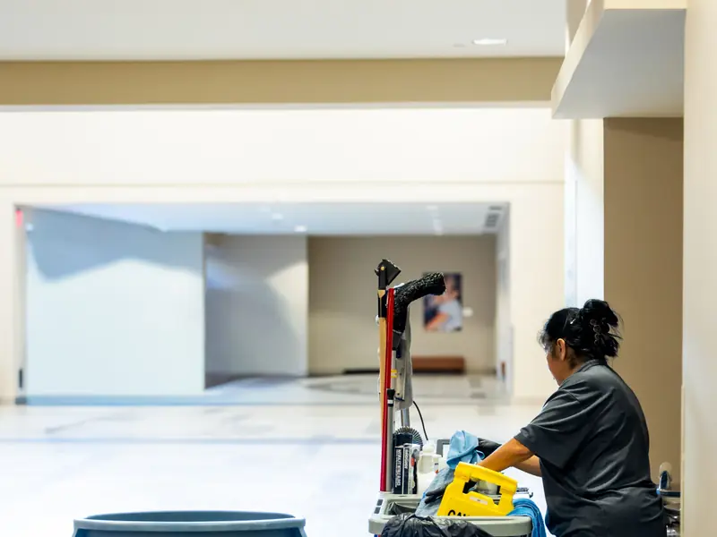 Profissional de limpeza com carrinho de materiais em corredor corporativo