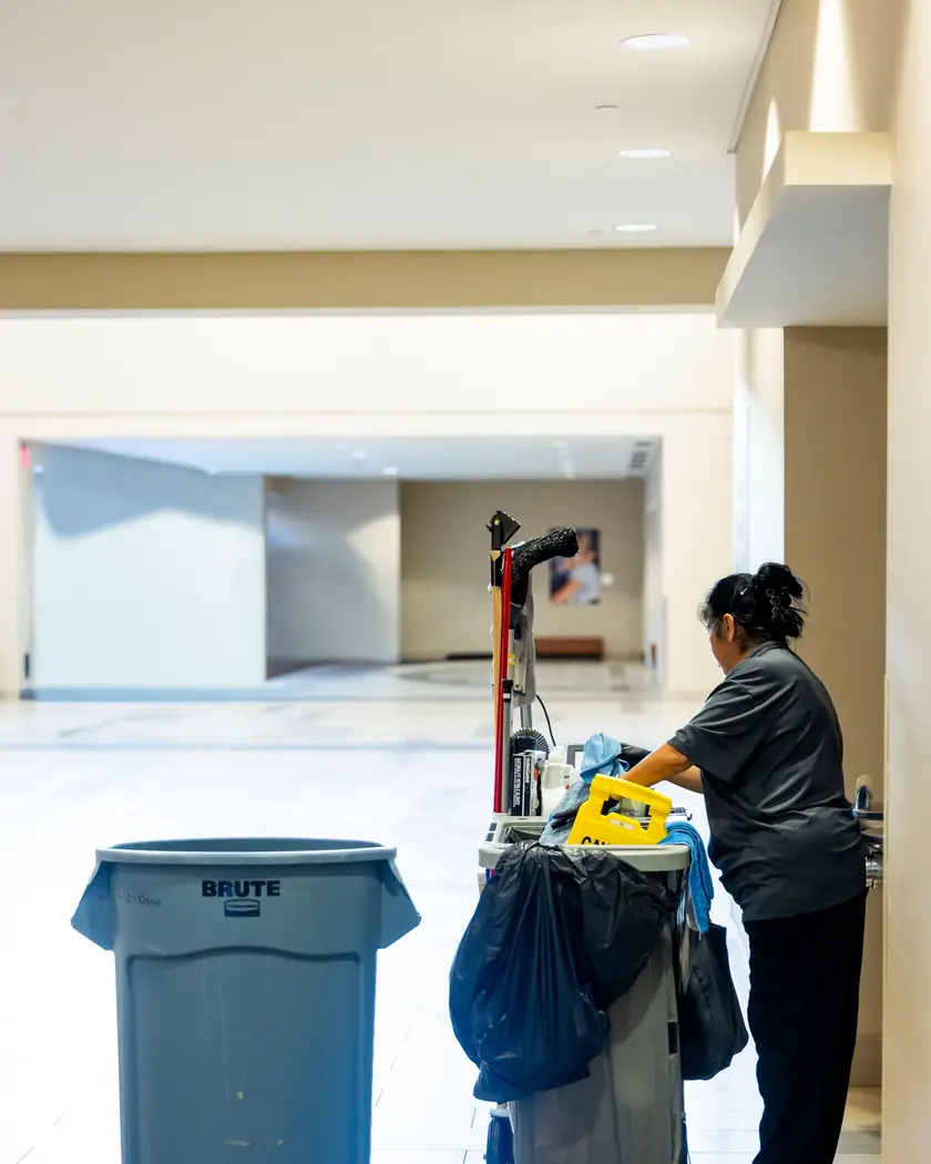 Profissional de limpeza com carrinho de materiais em corredor corporativo