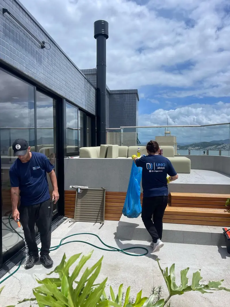 Dupla da equipe Uniq Serviços, de uniforme, realizando limpeza em terraço externo