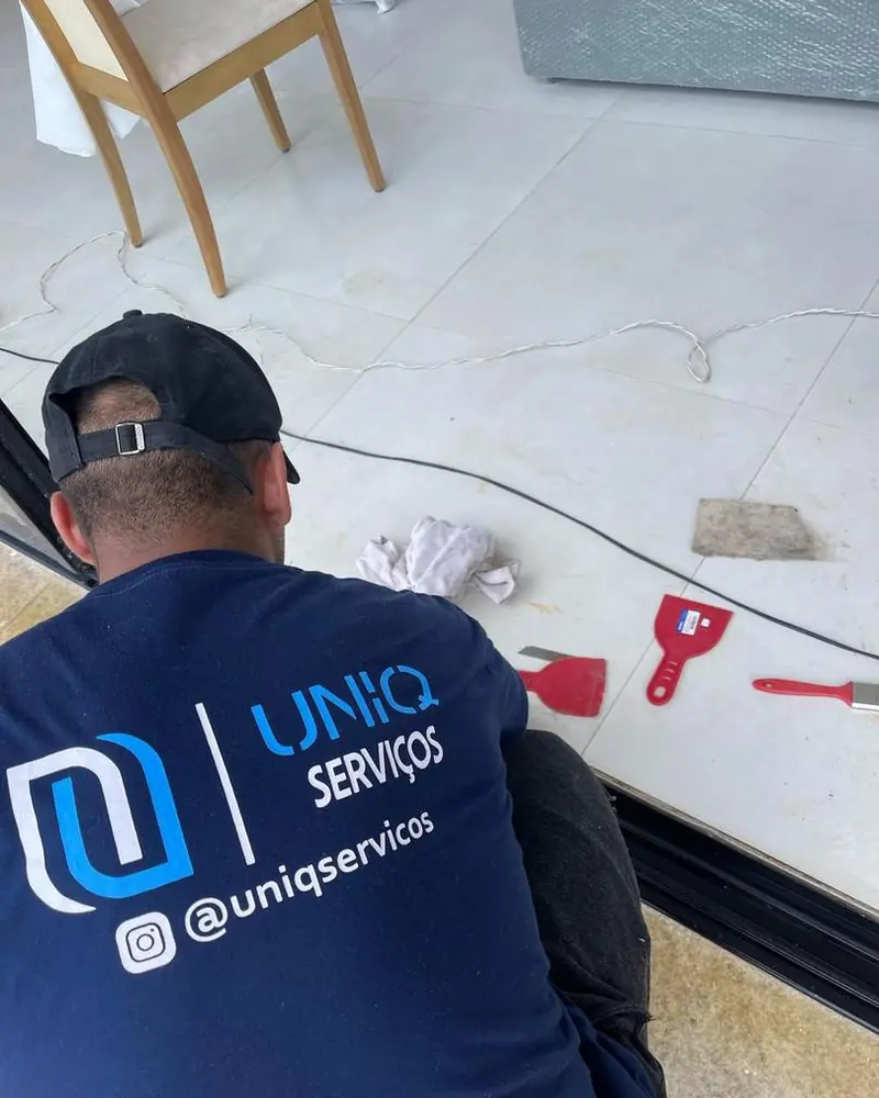 Profissional da Uniq Serviços, de uniforme, removendo resíduo de obra do piso com espátula